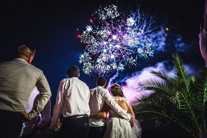 Un groupe de personnes, dont un couple, regarde un feu d'artifice coloré dans le ciel nocturne.