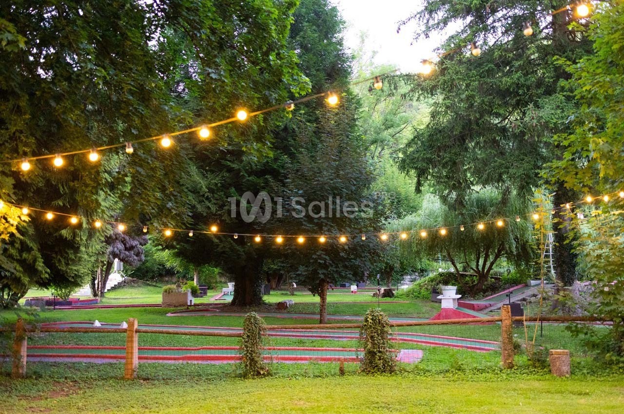 Terrain de mini-golf en plein air entouré d'arbres, éclairé par des guirlandes lumineuses suspendues.
