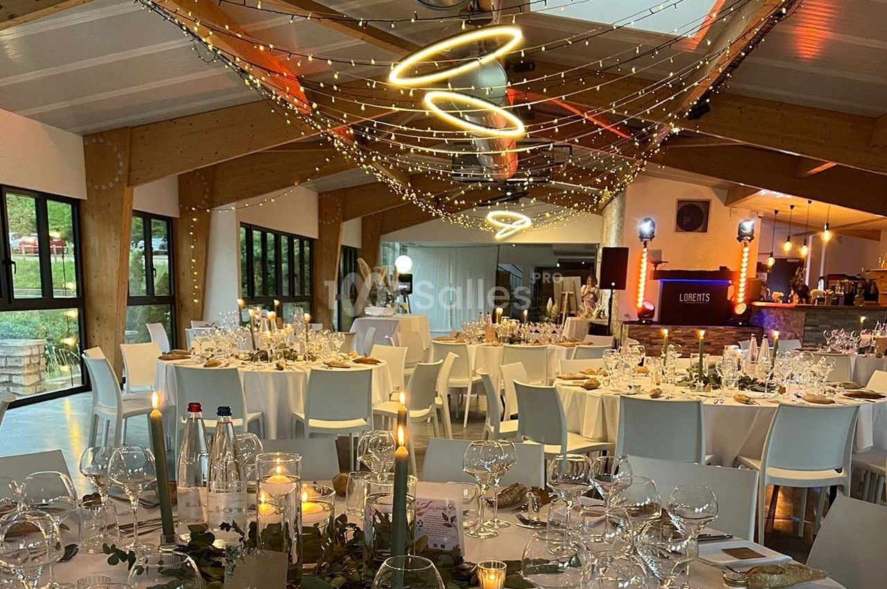 Salle de réception décorée avec des tables dressées, guirlandes lumineuses suspendues et ambiance chaleureuse.