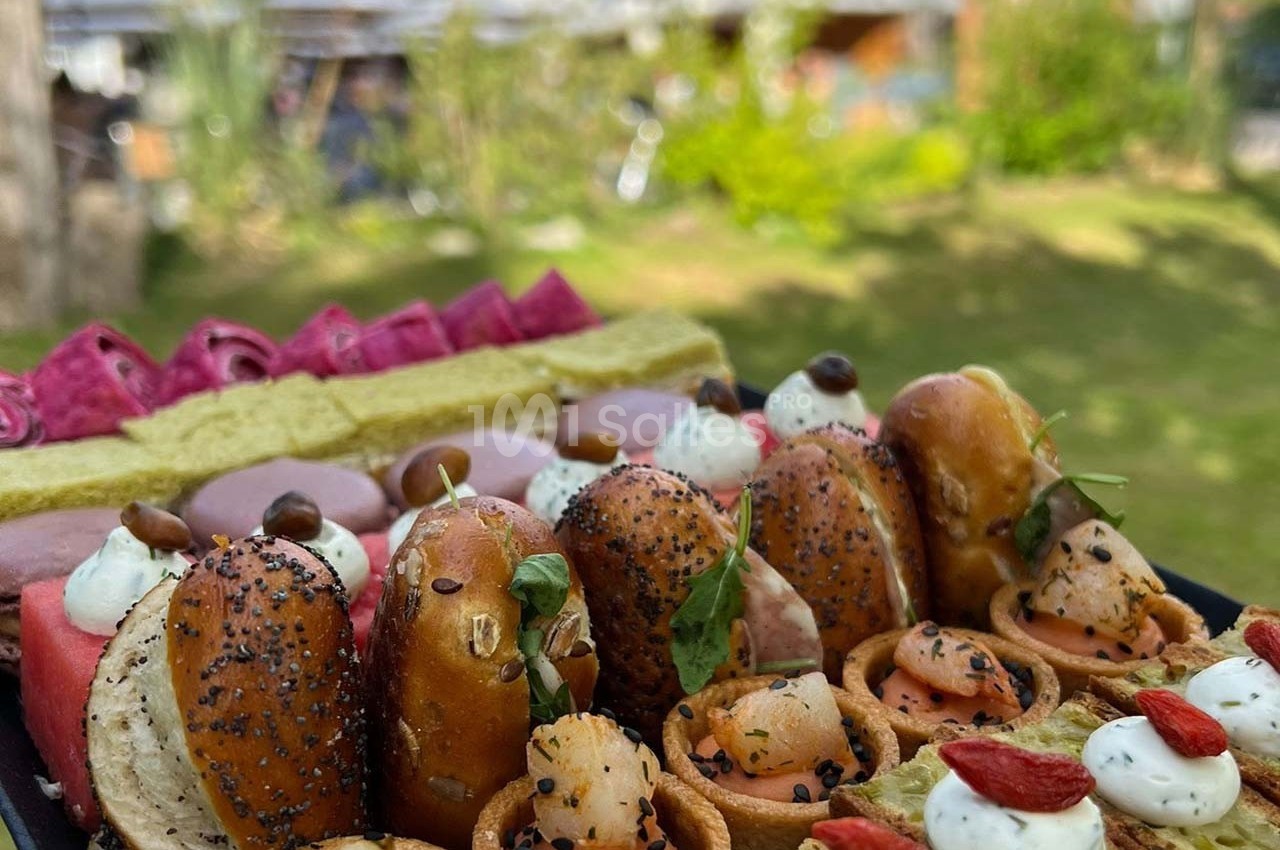 Plateau de bouchées variées comprenant mini-pretzels, saumon, fromage frais et garnitures colorées, en extérieur verdoyant.