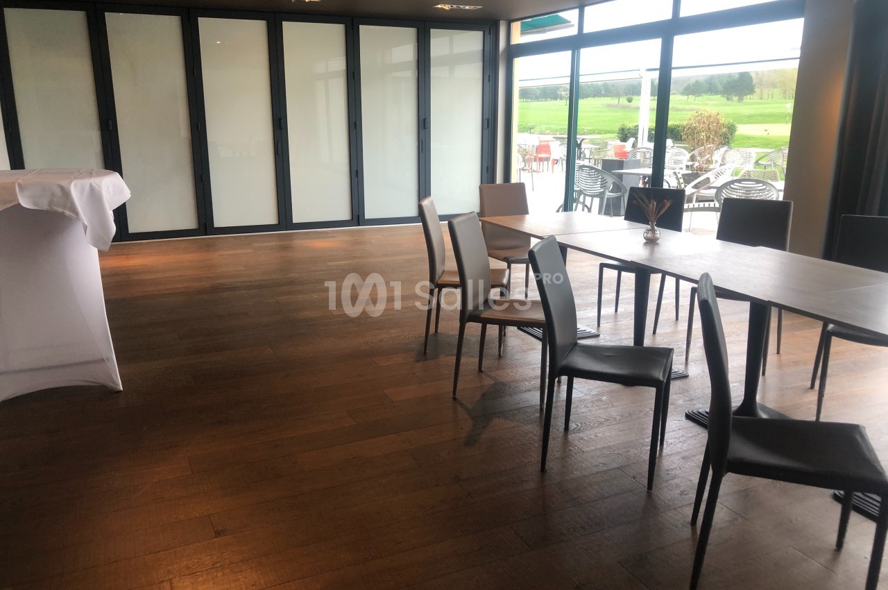 Salle lumineuse avec parquet en bois, tables et chaises modernes, grandes baies vitrées donnant sur une terrasse et un…
