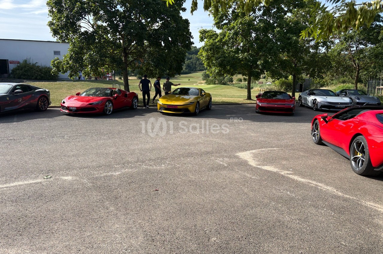 Plusieurs voitures de sport colorées garées en extérieur sur un parking entouré d'arbres.