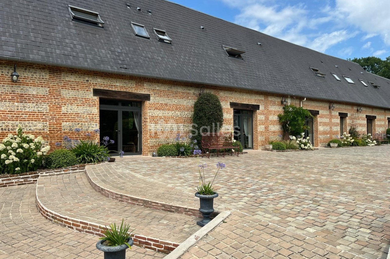 Façade en briques d'un bâtiment avec toit en ardoise, entourée de plantes et donnant sur une cour pavée.