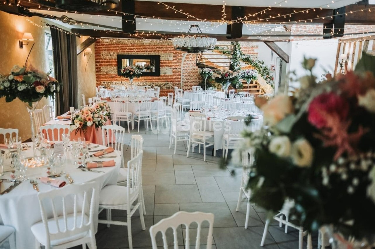 Salle de réception décorée avec des tables rondes, nappes blanches, chaises assorties et arrangements floraux élégants.