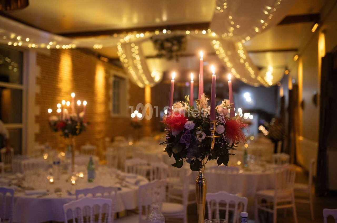 Bougeoir décoratif avec fleurs au centre d'une salle de réception éclairée par des guirlandes lumineuses.