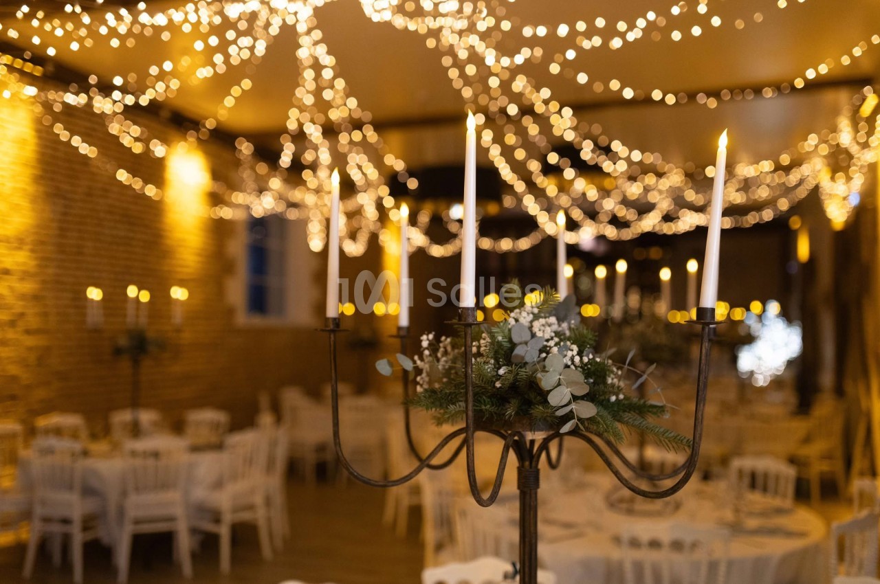 Salle de réception décorée avec des guirlandes lumineuses et un chandelier orné de feuillage et de bougies allumées.