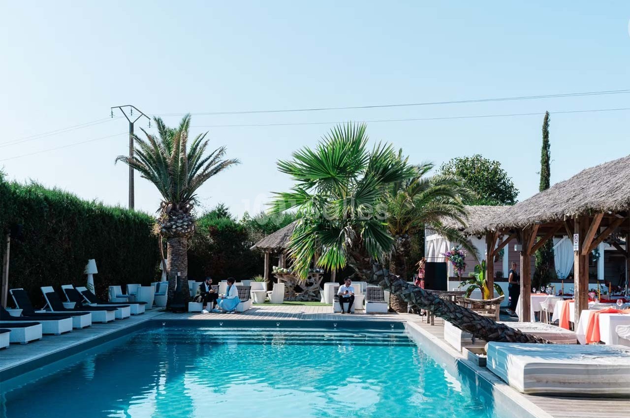 Piscine extérieure entourée de palmiers, transats et espaces de détente sous des toits en chaume.