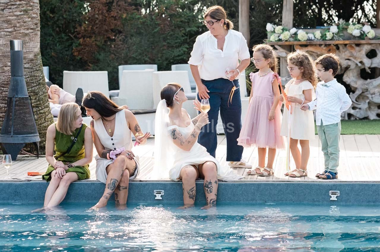 Des adultes et des enfants discutent et jouent au bord d'une piscine dans un cadre extérieur ensoleillé.