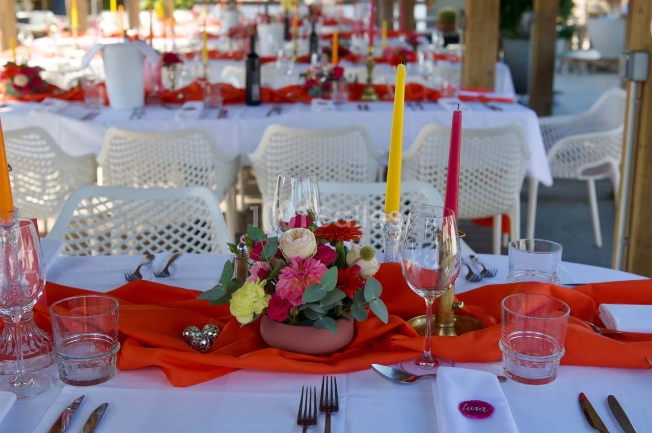Table dressée avec nappes blanches, chemins de table rouges, bougies colorées et centre de table floral.