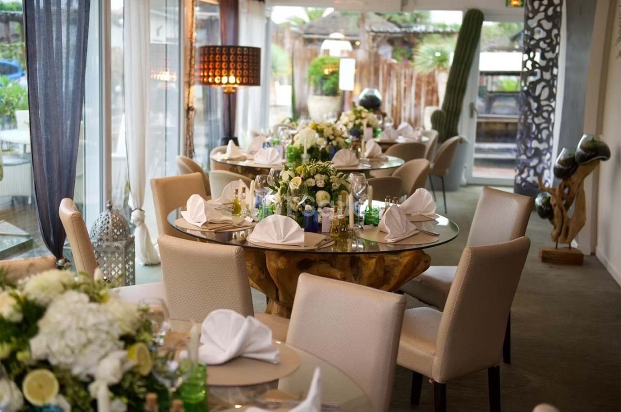 Salle de réception élégante avec tables rondes décorées de fleurs blanches et serviettes pliées, ambiance lumineuse.
