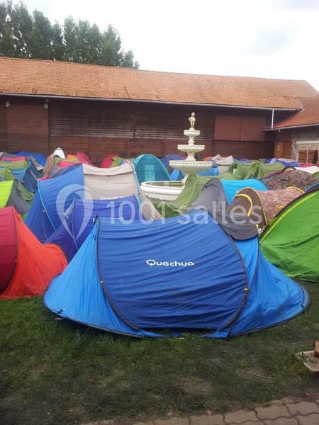 Tentes colorées installées sur une pelouse près d'un bâtiment en briques avec une fontaine blanche au centre.