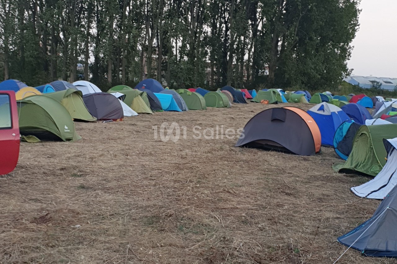 Plusieurs tentes colorées installées sur un terrain herbeux entouré d'arbres.