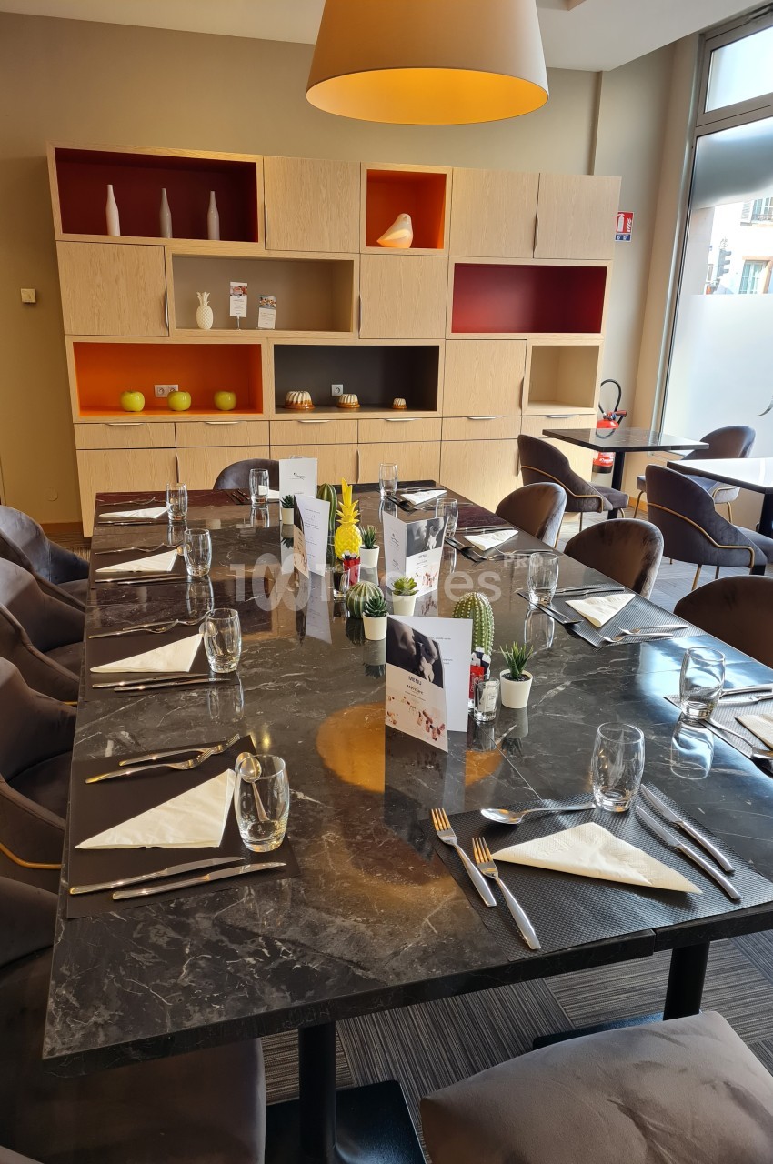 Table dressée avec vaisselle et menus dans une salle de restaurant moderne, éclairée par une grande baie vitrée.