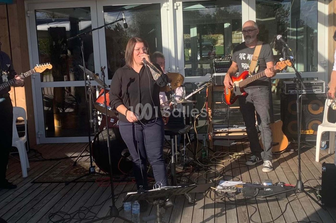 Un groupe de musiciens joue en plein air sur une terrasse en bois, avec une chanteuse au centre.