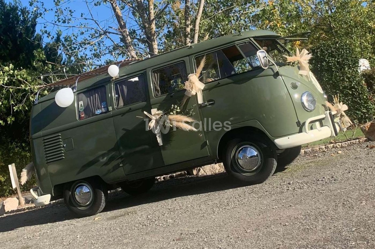 Combi Volkswagen vert décoré de fleurs séchées et de ballons blancs, stationné sur un chemin gravillonné.