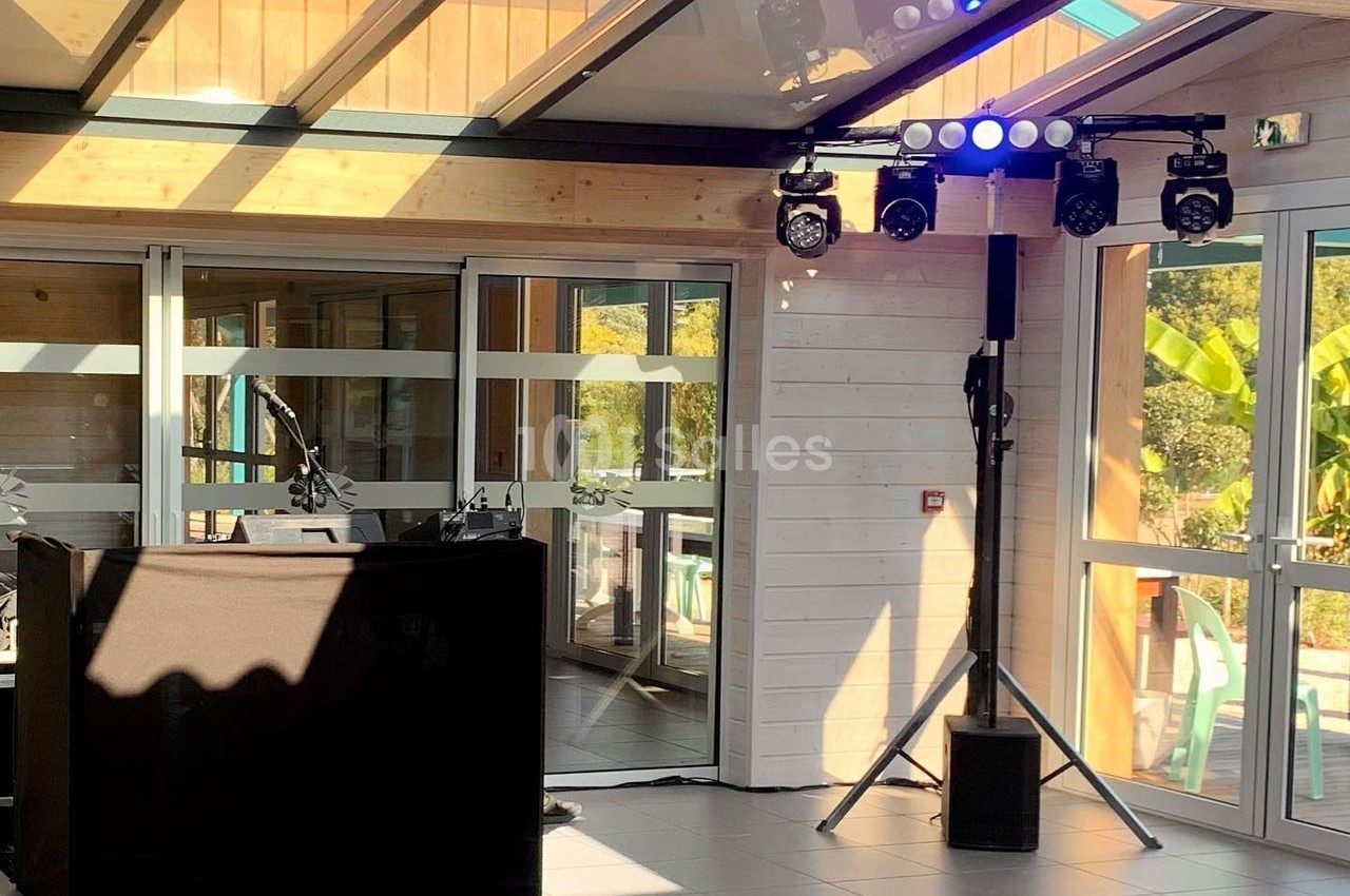 Installation de matériel de sonorisation et éclairage dans une salle lumineuse avec baies vitrées et structure en bois.