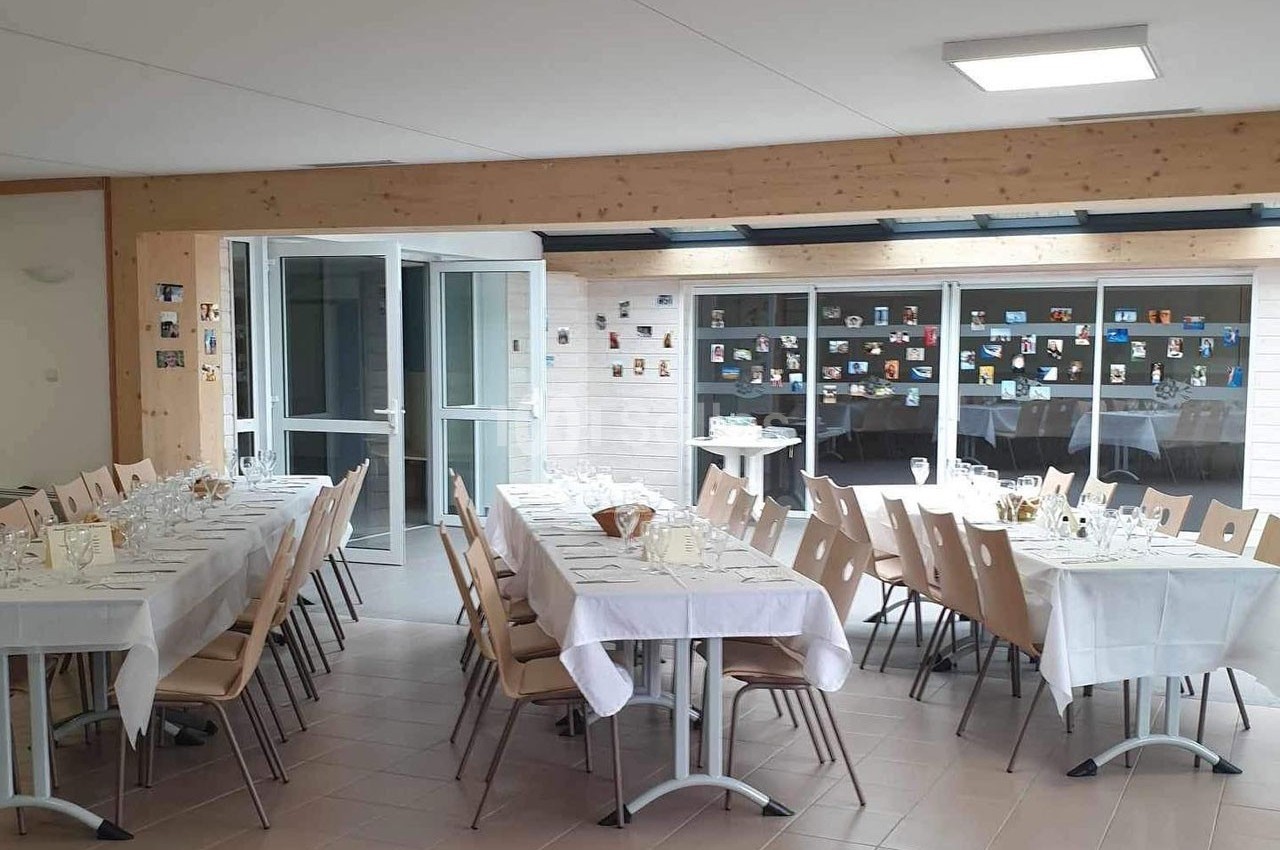 Salle lumineuse aménagée pour un repas, avec des tables dressées et des chaises, décorée de photos au mur.