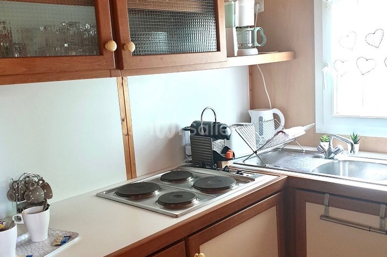 Cuisine lumineuse avec plaques de cuisson, évier, machine à café et rangements en bois clair.