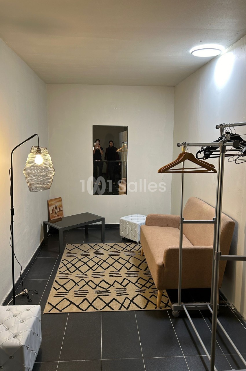 Salle minimaliste avec canapé beige, miroir, portants à vêtements, tapis géométrique et lampe suspendue.