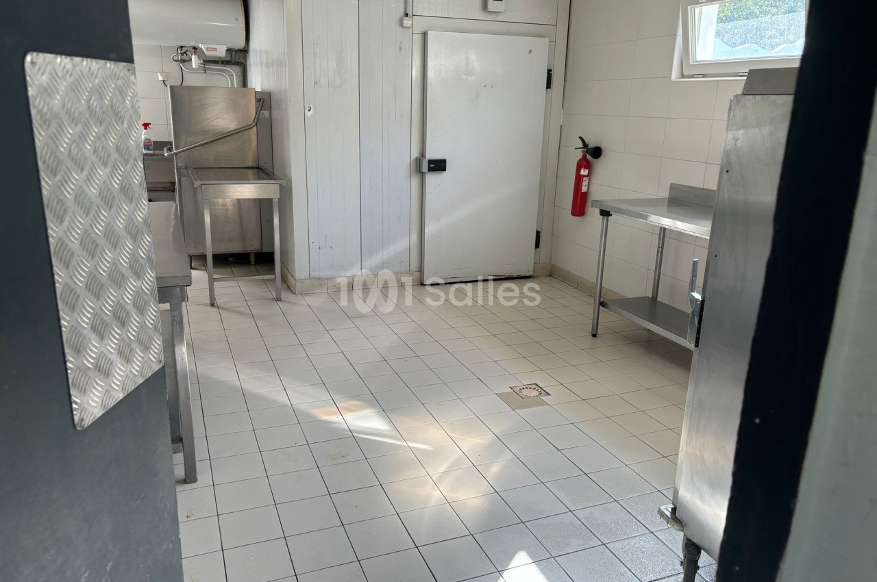 Cuisine professionnelle vide avec équipements en inox, sol carrelé, porte froide et extincteur fixé au mur.