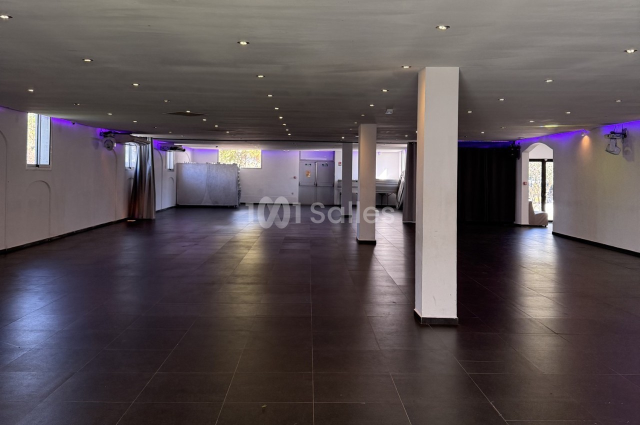 Salle spacieuse avec sol en carrelage sombre, murs blancs, éclairage au plafond et lumières violettes en périphérie.