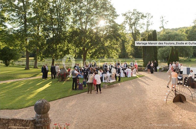 Groupe de personnes rassemblées dans un jardin pour une réception en plein air, entouré d'arbres et de pelouses.