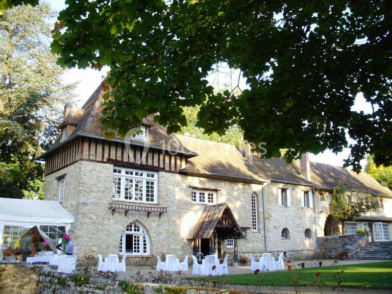 Manoir en pierre entouré de verdure avec des tables et chaises blanches installées sur la pelouse.