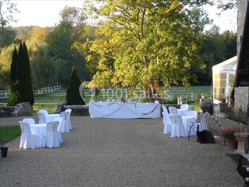 Cour extérieure aménagée pour un événement, avec des tables et chaises blanches, et une table décorée au fond.