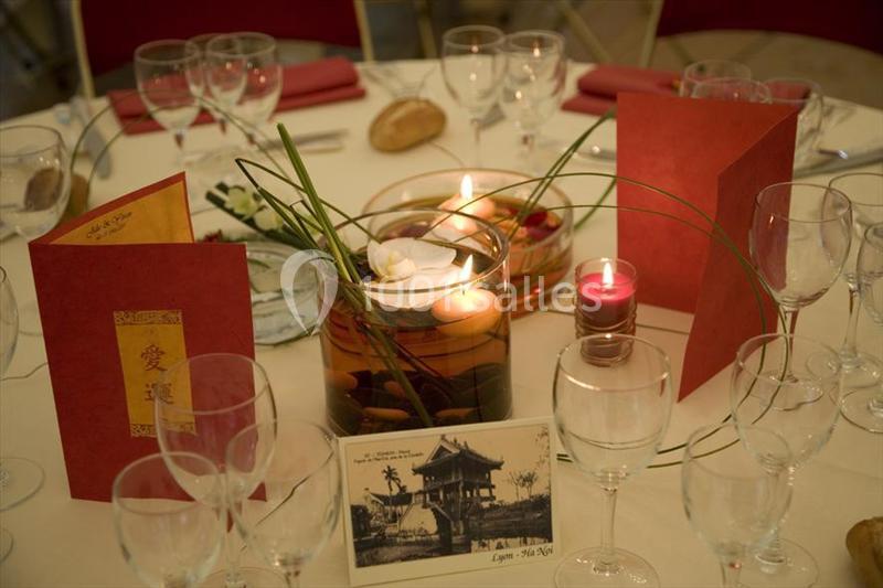 Table dressée avec des verres, menus rouges, bougies flottantes dans un vase et une carte postale en décoration.