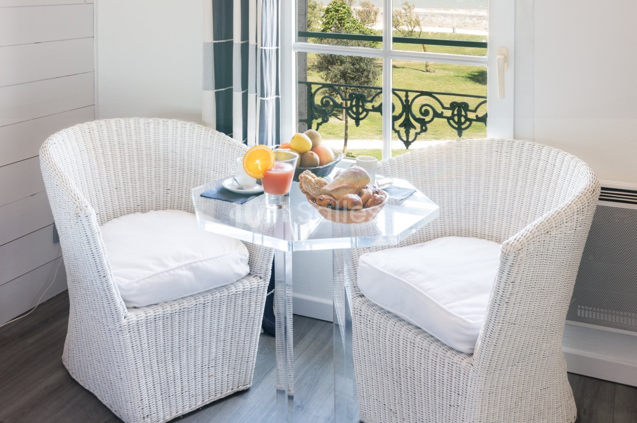 Deux fauteuils en rotin blanc autour d'une table avec un petit-déjeuner, près d'une fenêtre donnant sur un parc.