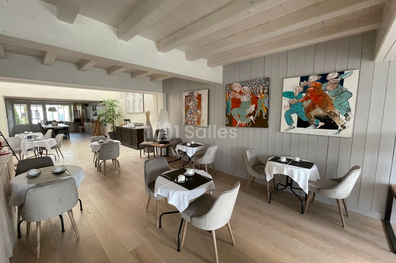 Salle de restaurant lumineuse avec tables dressées, chaises modernes et peintures colorées accrochées aux murs.