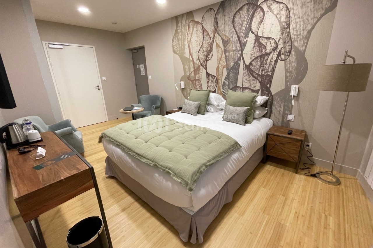 Chambre d'hôtel moderne avec lit double, bureau en bois, fauteuils, lampadaire et décoration murale abstraite.