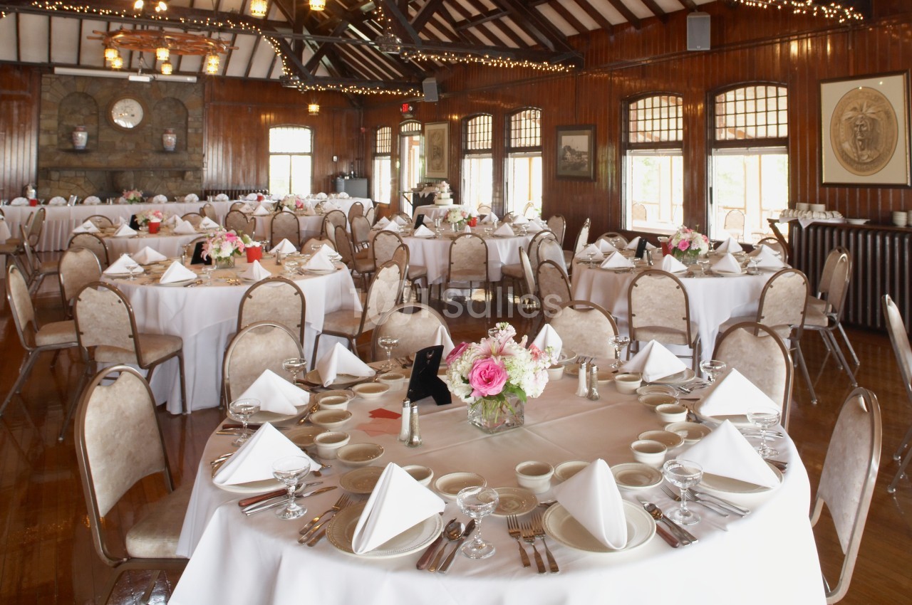 Salle de réception avec tables rondes dressées, nappes blanches, serviettes pliées et décorations florales.