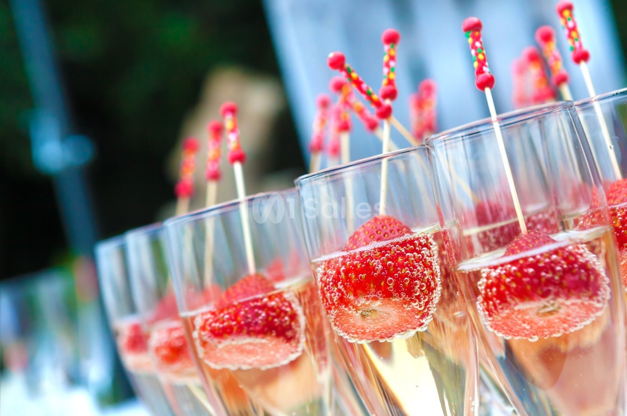 Verres de champagne garnis de fraises et décorés de bâtonnets colorés, alignés sur une table.
