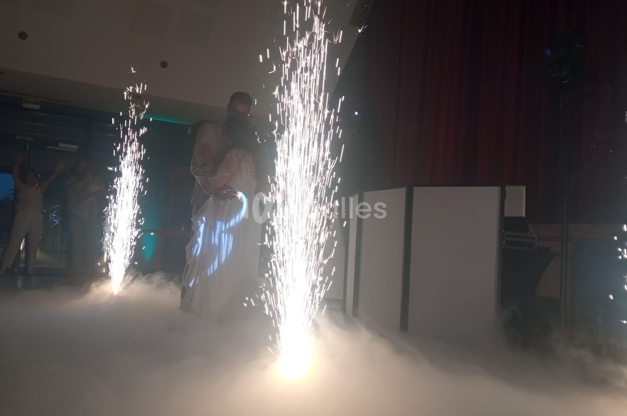 Un couple danse au milieu d'effets pyrotechniques et d'une ambiance de fumée dans une salle sombre.