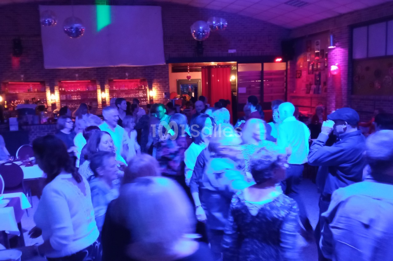 Groupe de personnes dans une salle éclairée par des lumières colorées, certaines dansent, d'autres discutent.