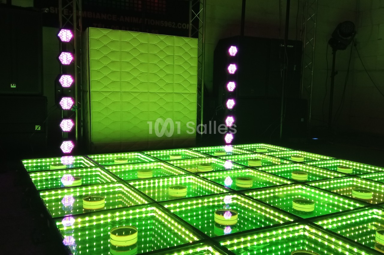 Piste de danse lumineuse avec des carreaux verts réfléchissants et des colonnes de lumières LED violettes.