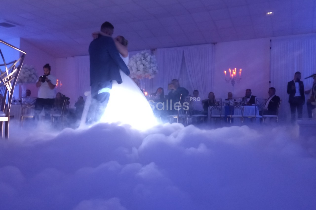 Un couple danse dans une salle de réception éclairée, entouré d'un effet de fumée au sol.