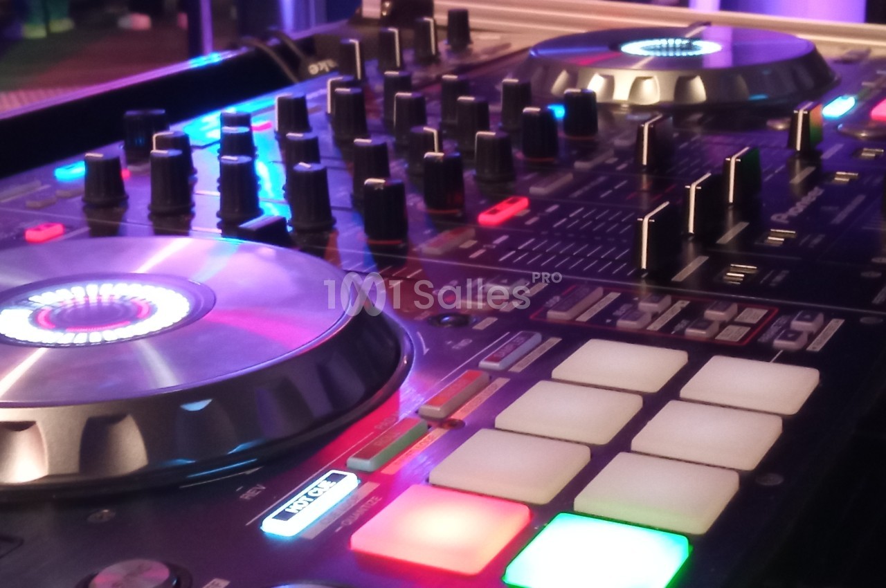 Table de mixage DJ avec platines lumineuses, boutons de réglage et pads colorés dans un environnement éclairé.