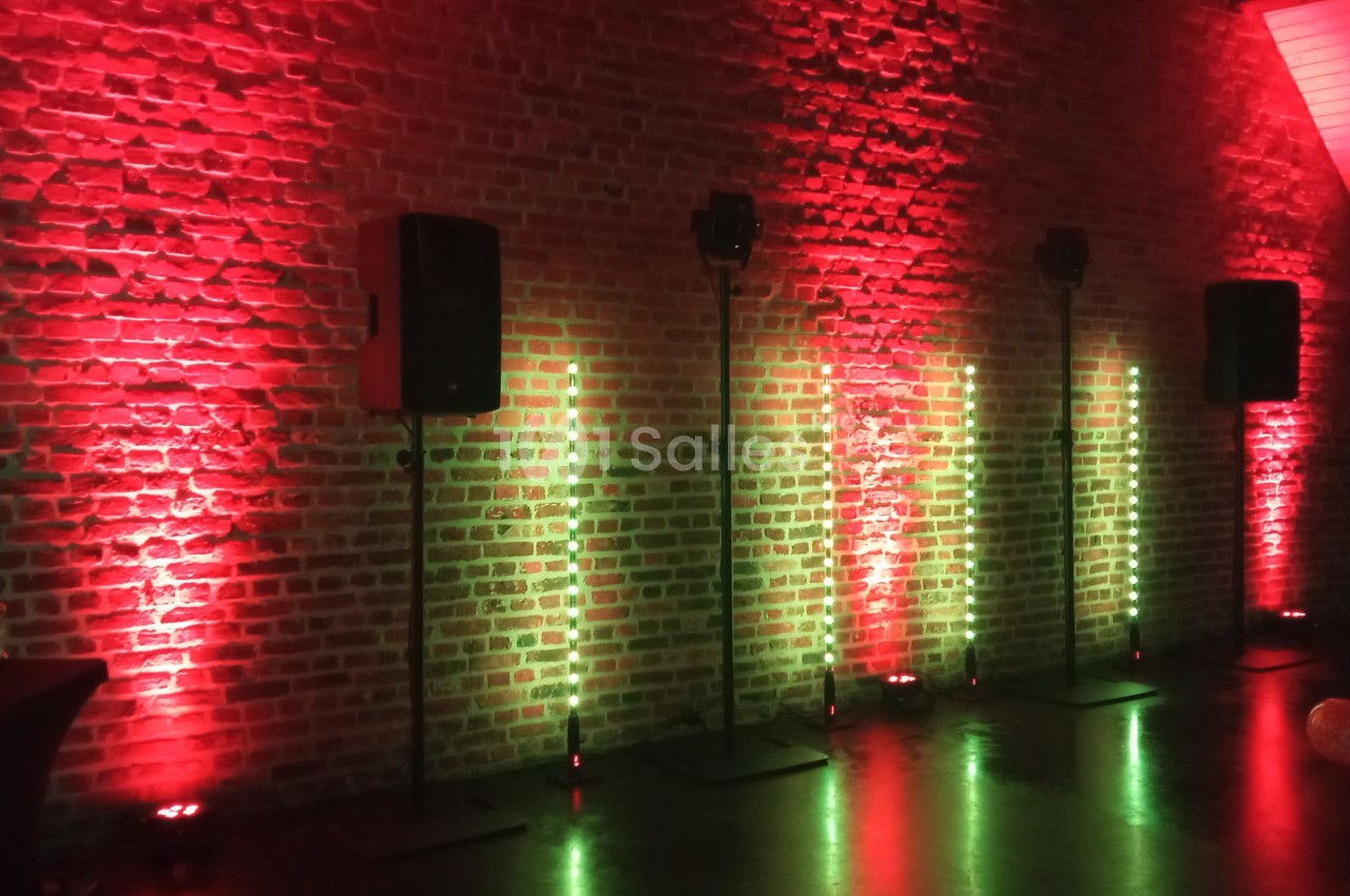 Mur en briques éclairé par des lumières rouges et vertes avec des enceintes noires sur pieds alignées.