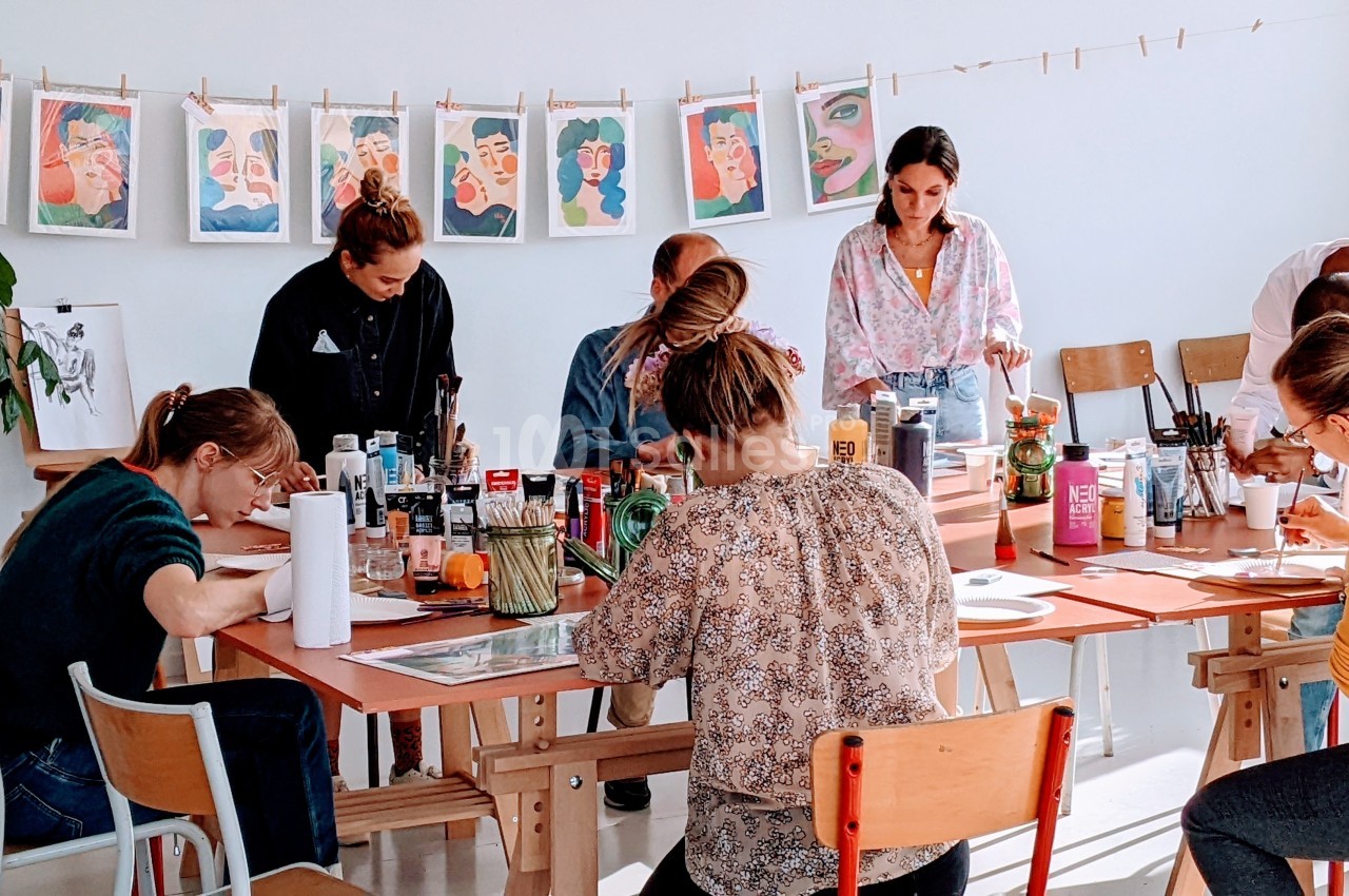 Des personnes participent à un atelier artistique, dessinant et peignant autour d'une grande table dans une salle lumineuse.