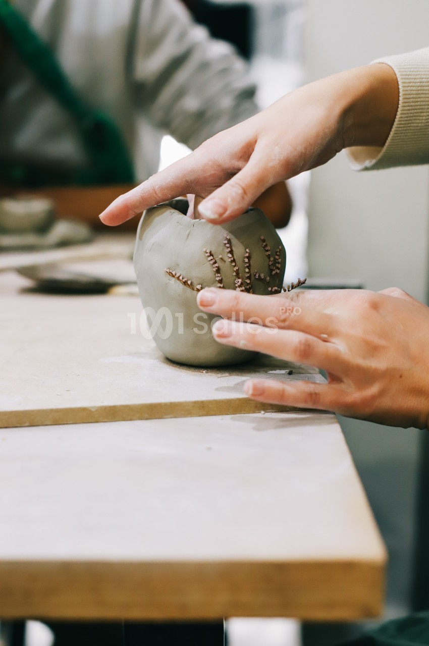 Deux mains façonnent une pièce en argile ornée de motifs, posée sur une table de travail.