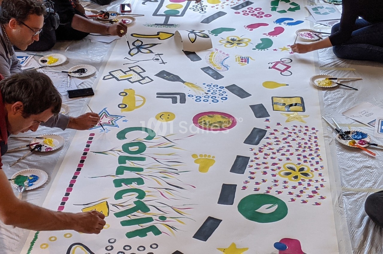 Des personnes peignent ensemble une grande fresque colorée avec des motifs variés et le mot ’COLLECTIF’ au centre.