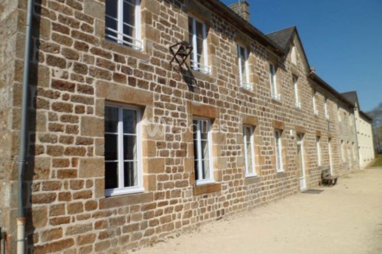 Façade en pierre d'une maison traditionnelle avec plusieurs fenêtres blanches, sous un ciel bleu clair.