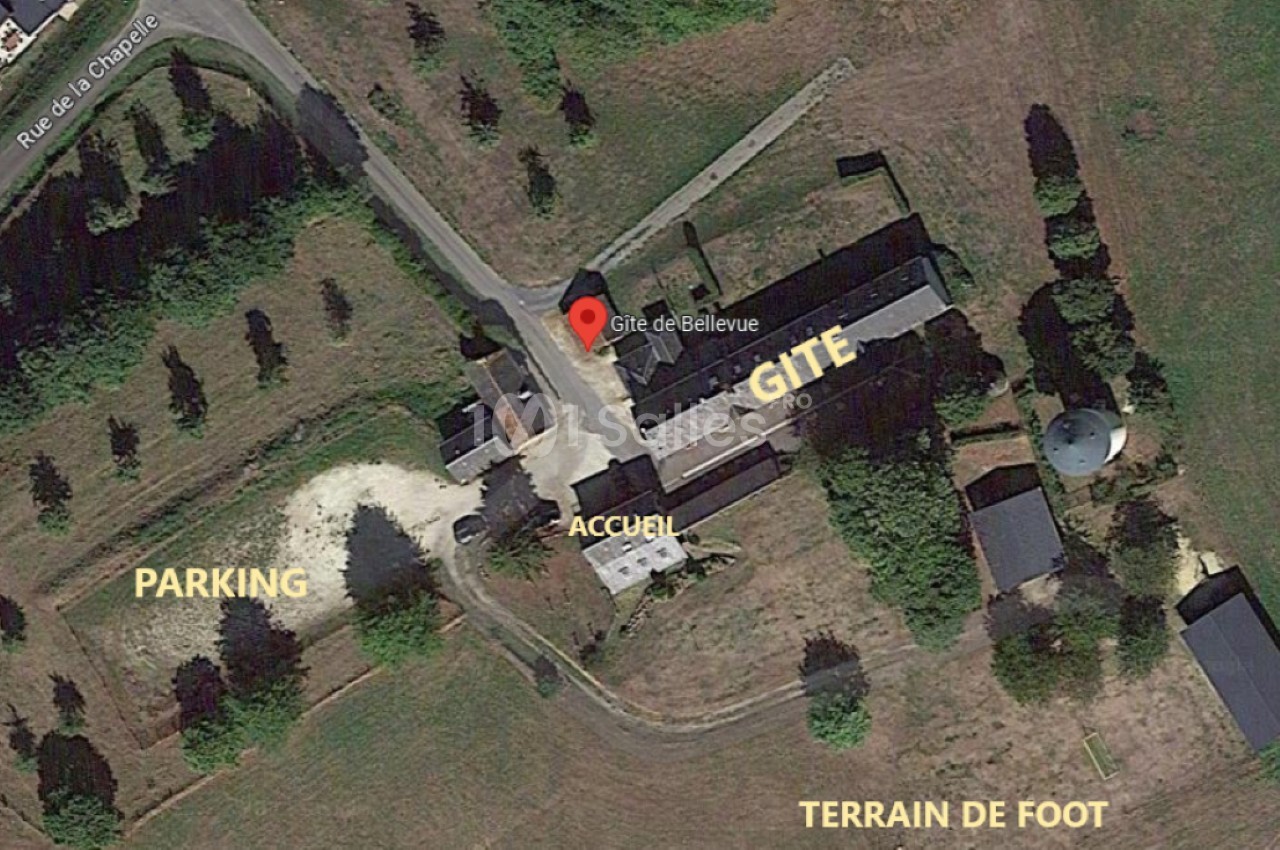 Vue aérienne d'un gîte avec parking, terrain de football et bâtiments entourés de verdure.