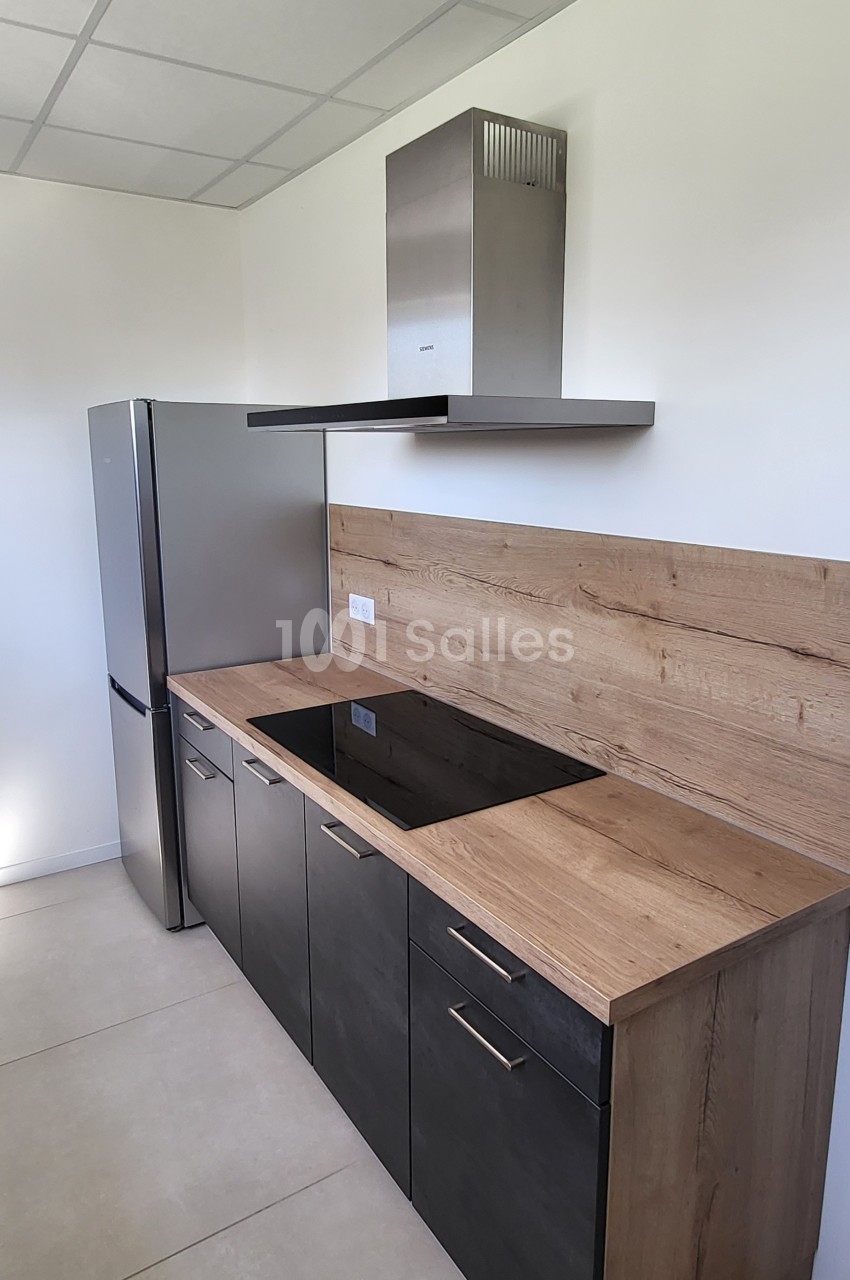 Cuisine moderne avec plan de travail en bois, plaques de cuisson noires, hotte en inox et réfrigérateur argenté.