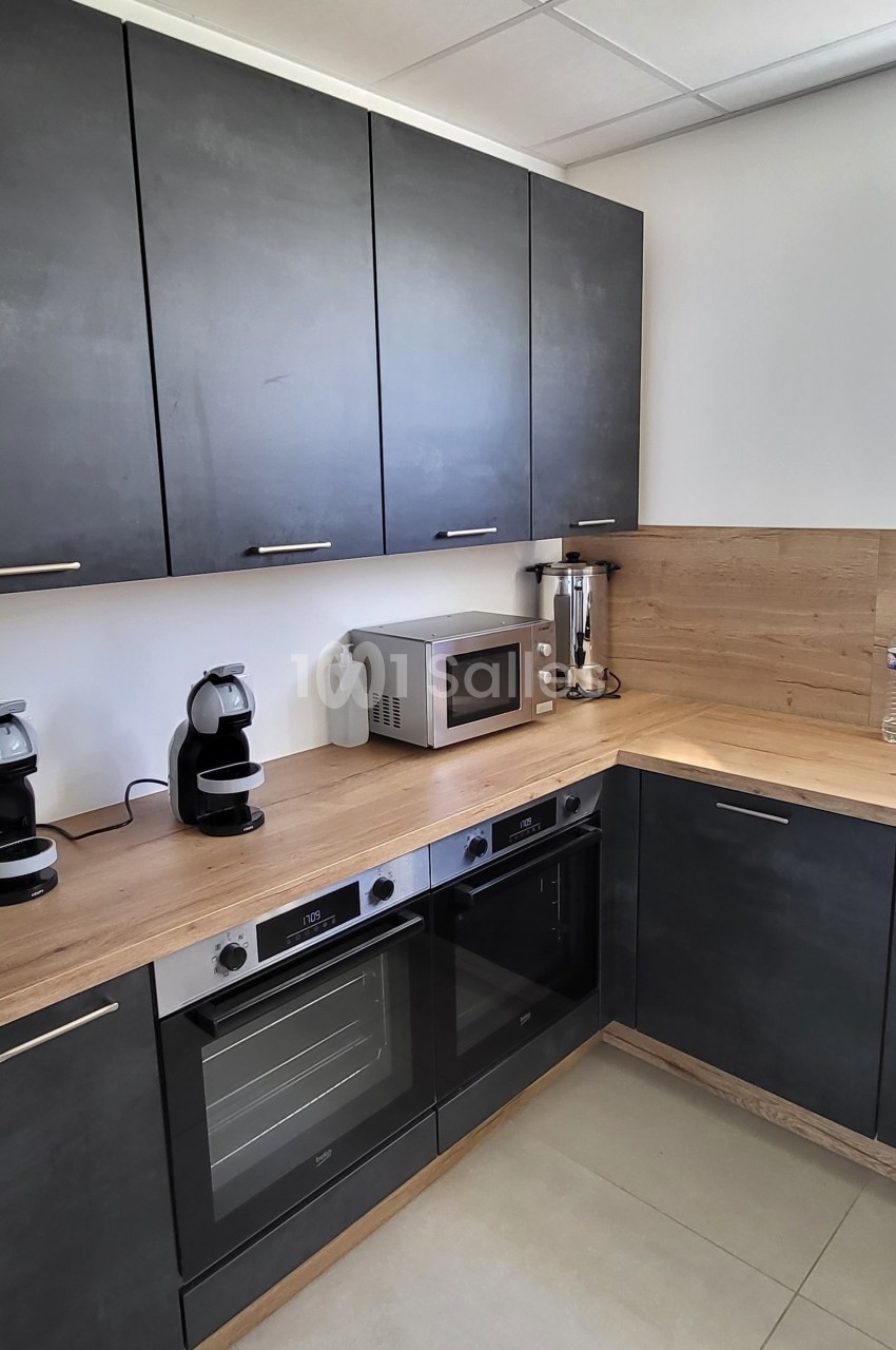 Cuisine moderne avec meubles noirs, plan de travail en bois clair, électroménager intégré et carrelage beige au sol.
