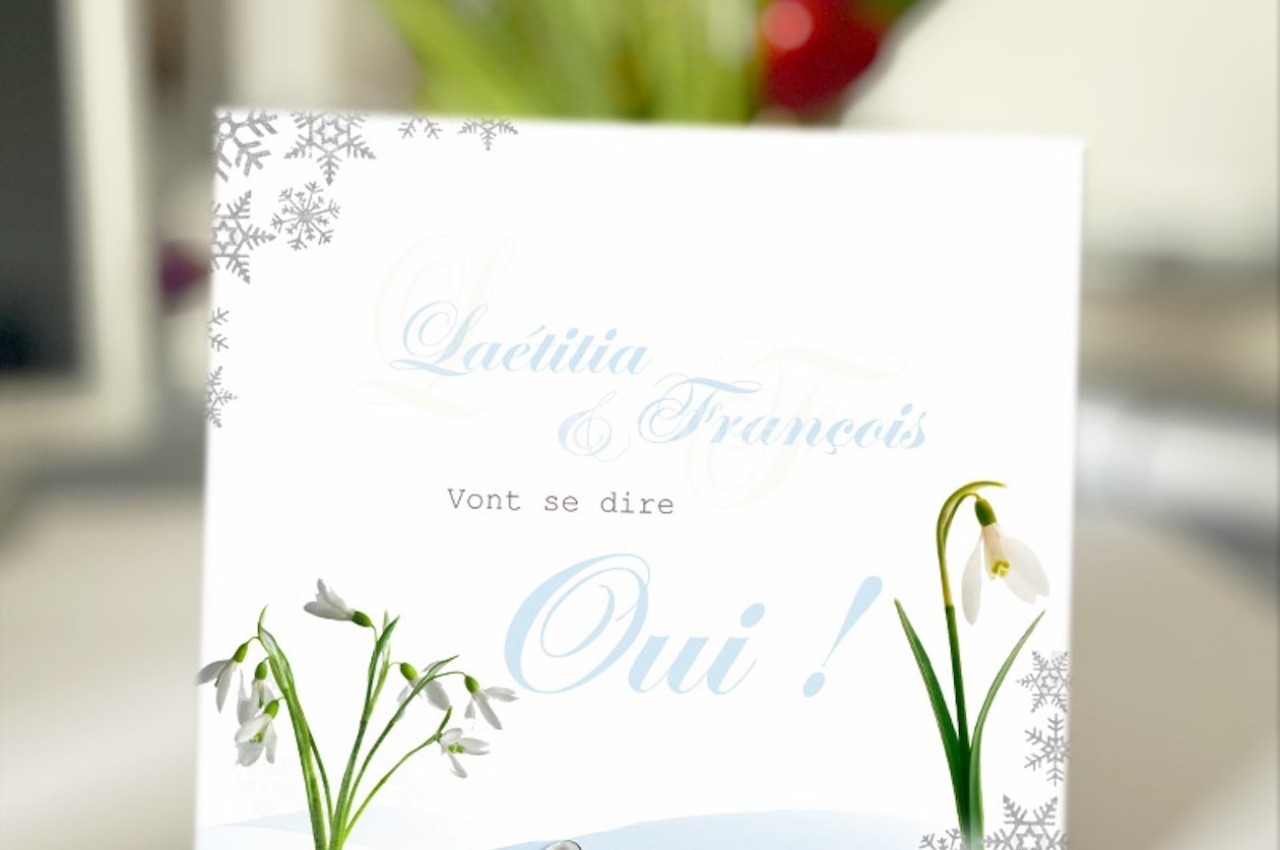Carte avec des perce-neige, des alliances et le texte ’Laetitia & François vont se dire Oui !’ sur fond flou.