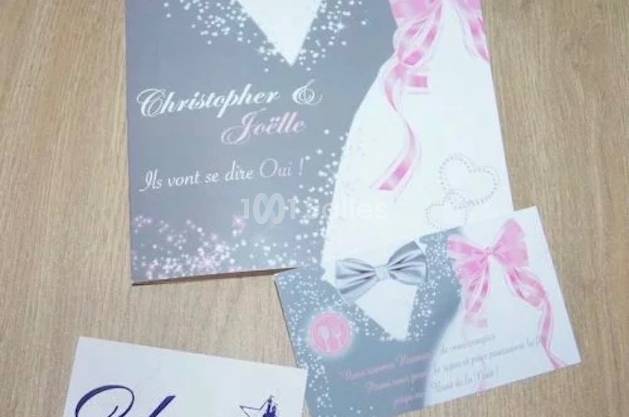 Carte d'invitation de mariage avec nœuds roses et argentés, posée sur une table en bois avec une carte de visite.