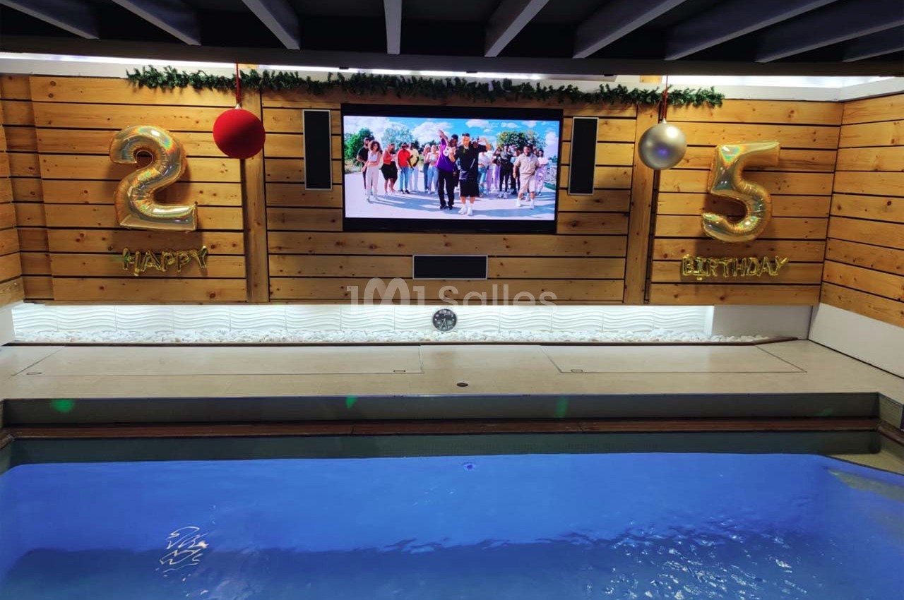 Piscine intérieure avec écran mural, décorations d'anniversaire ’25’ dorées et boules suspendues.